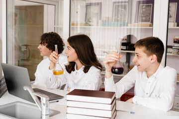 Pupils holding flasks with liquid for experiments in laboratory. Education concept. Group of pupils studying chemistry lesson in school.