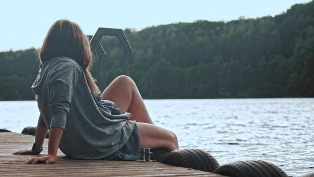 Young Caucasian Woman Sitting on Wooden Pier Quay Looking at Calm Lake and Forest