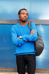 Bored guy wearing a blue sweater and carrying a backpack stands at a bus stop waiting for a bus 