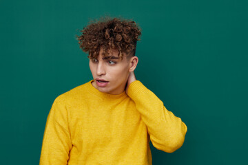 Fototapeta na wymiar a shocked man in a yellow sweater stands on a green background and holds his head with his hand, his mouth wide open, looking away. Horizontal photo