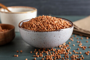 Bowl with buckwheat grains on color wooden table