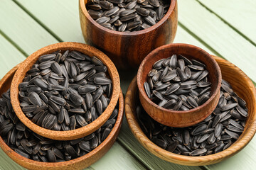 Bowls of black sunflower seeds on green wooden background