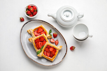 Plate with delicious strawberry puff pastry, teapot and cups on light background