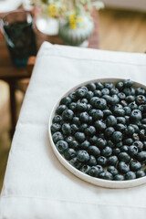 Fresh blueberries on modern ceramic plate and wildflowers bouquet in rustic room. Summertime in countryside. Healthy food aesthetics. Summer berries