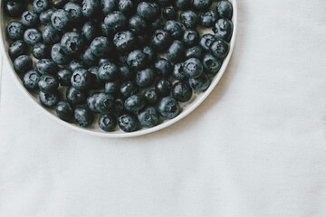 Blueberries in modern ceramic plate flat lay. Summertime in countryside. Healthy food aesthetics. Summer berries on soft linen background, moody banner