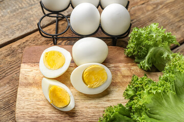 Board with boiled chicken eggs and lettuce on wooden background, closeup