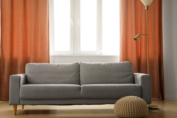 Grey sofa, pouf and standard lamp near red curtains in room