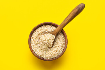 Wooden bowl with spoon and sesame seeds on yellow background