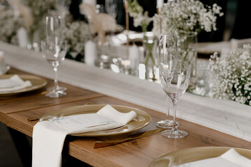 Aesthetic table setting in the restaurant for the holiday with flowers and gold, glasses