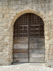 Fototapeta na wymiar Brown wooden door surrounded by stone arch on side of ancient stone building