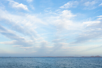 Naklejka na ściany i meble Blue sky with white spindrift clouds under sea waves