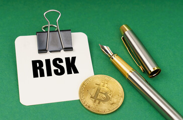 On a green surface, a bitcoin coin, a pen and a sheet of paper with the inscription - Risk - Powered by Adobe