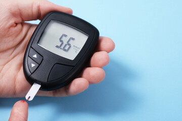 Woman using glucometer, checking blood sugar level. Diabetes concept on blue background. The glucometer shows a normal sugar level.