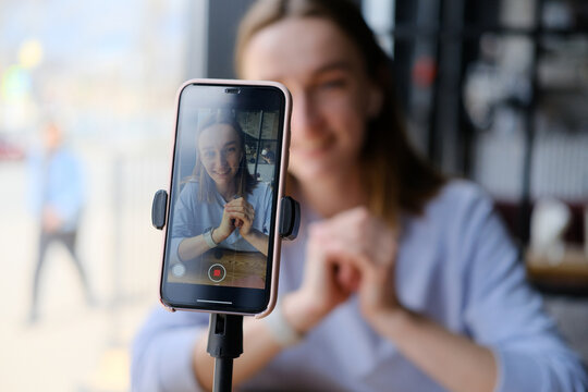 Young beautiful woman blogger making a video for her blog using phone camera in a cafe.