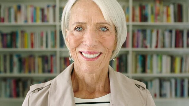 Face portrait of happy senior woman with library. Smart, wise and enlightened mature female. Big collection of books in home office for a teacher or professor. Knowledgable on various topics