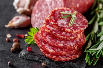Traditional smoked salami sausage with spices.Salami sausage slices on a black chopping Board. Dark background.