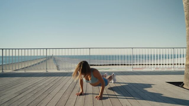 Sportswoman workout outdoor on seaside - she make burpee exercise. High quality 4k footage