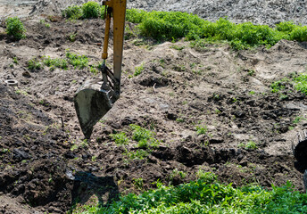 Excavator bucket on the background of broken ground and green grass