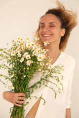 Young slim white curly woman holding huge bouquet of daisies with pleasure. Wind blows hair. Field daisies for soothing herbal and natural beauty drink. Acceptance of loneliness. Mental health care.