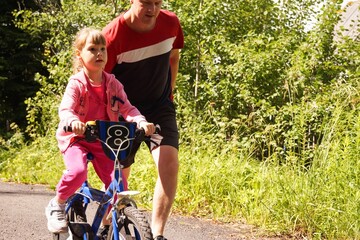 Father teaches his daughter to ride bicycle in park.