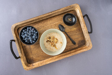 Healthy breakfast of cooked oatmeal with fresh walnuts and blueberries, served on a rustic wooden tray

