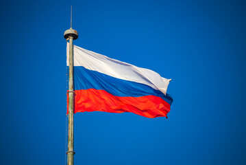 Russian flag in the bright blue sky on high flagpole.