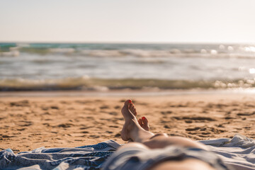 the feet of a woman lying on a towel on the beach near the sea