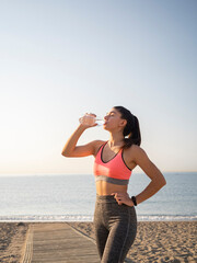 Girl athlete taking a break during the race to hydrate during exercise on the beach. Active and...
