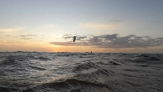 sunrise on the beach, kiter water sport enthusiast infront of clouds and sunset, 4k slow motion portrait mode