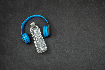 sport concept, Backlit plastic water bottle with blue wireless headphone on grunge background
