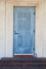 Old blue door with peeling and cracked blue paint against white wall