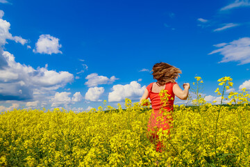 Young pretty woman in a colored dress on Lightning cheerful yellow background blooming rapeseed...