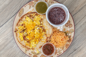 Overhead view of thick homemade tortilla holds a breakfast taco covered with melted cheese, cilantro and salsa dipping sauce for a fullfilling meal