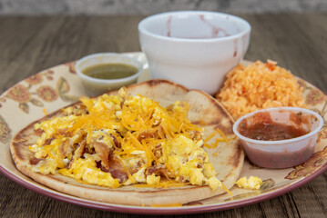 Thick homemade tortilla holds a breakfast taco covered with melted cheese, cilantro and salsa dipping sauce for a fullfilling meal