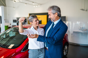 Beautiful middle-aged smiling couple holding a key of their new car.