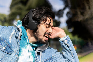 Young latin man listening to music outdoors with headphones. Expression of happiness, winning attitude.