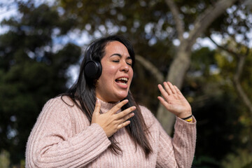 Young latin woman listening to music outdoors with headphones. Expression of happiness, winning attitude. Copy space