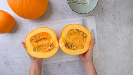 Woman cuts fresh ripe orange pumpkin into slices on grey stone background