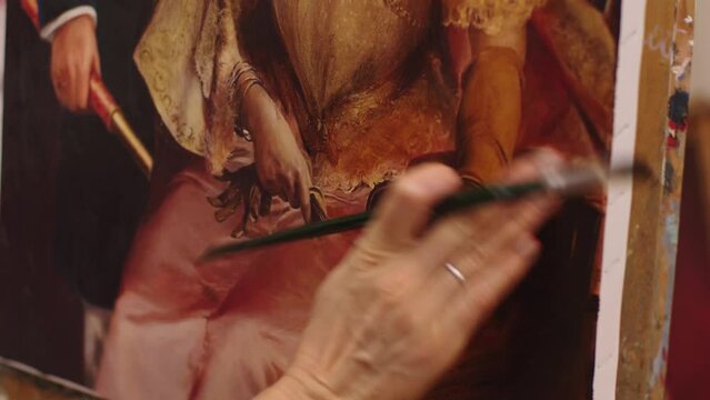 Female hand is laiding the brush strokes on canvas. close-up of artist hand with paintbrush drawing the portrait of woman in the art workshop. portrait painting techniques.