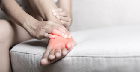 Foot pain, Asian woman sitting on sofa hold her ankle injury feeling pain in her foot at home,...