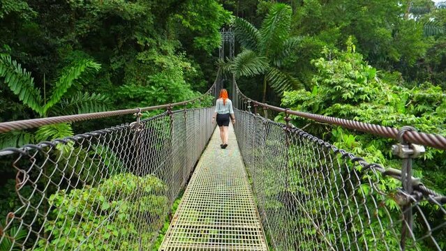 Slow-motion moves forward shot, a woman walking the hanging bridge of La Fortuna in the middle of the rain forest in Costa Rica.