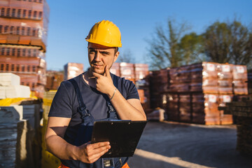 One man construction worker standing at warehouse or on the site holding clip document checking...