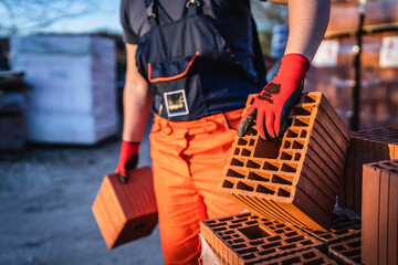 Close up on hands and midsection of unknown man construction worker taking clay brick blocks ar warehouse or construction site in sunny summer day copy space
