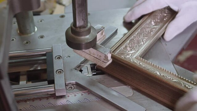 Close-up of hands in gloves, fixing the angle of wooden picture frame. making of carving pattern on corner of frame with special pressing equipment.