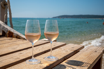 Glasses of cold rose wine from Provence served outdoor on wooden yacht pier with view on blue water and white sandy beach Plage de Pampelonne near Saint-Tropez, France