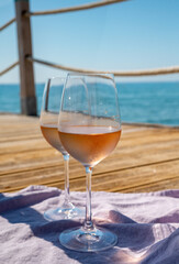 Glasses of cold rose wine from Provence served outdoor on wooden yacht pier with view on blue water and white sandy beach Plage de Pampelonne near Saint-Tropez, France