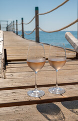 Glasses of cold rose wine from Provence served outdoor on wooden yacht pier with view on blue water and white sandy beach Plage de Pampelonne near Saint-Tropez, France