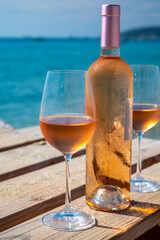 Glasses and bottle of cold rose wine from Provence served outdoor on wooden yacht pier with view on blue water and white sandy beach Plage de Pampelonne near Saint-Tropez, France