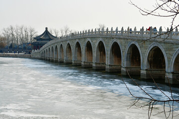 a traditional Chinese style arch bridge on the frozen lake in winter, Beijing, China