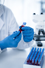 Doctor hand taking a blood sample tube from a rack with machines of analysis in the lab background, Technician holding blood tube test in the research laboratory. © PaeGAG
